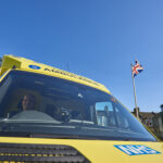 The front cab of an ambulance parked in an ambulance station with sunny blue sky in the background