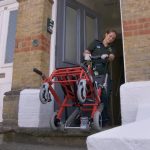 Clinician wheeling a chair into a patients home.